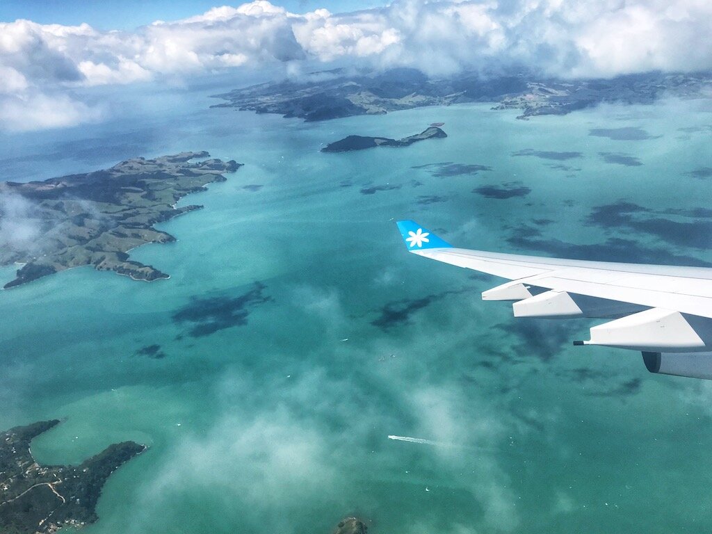 plane wing over a turquoise ocean and New Zealand islands