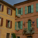 terracotta orange and yellow stone buildings with colorful shutters and white flowers draping from windows