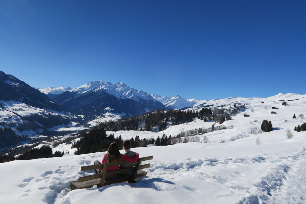 couple sitting on a bench high on a snowy mountain to experience winter in Europe