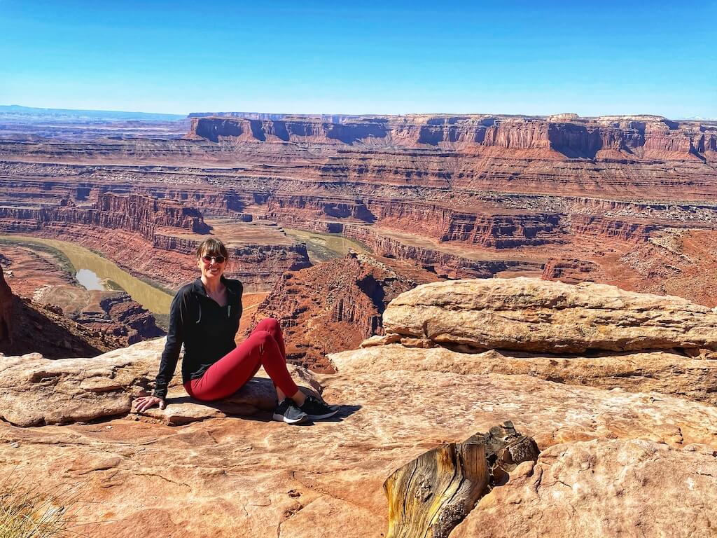 Woman sitting on a rock with Colorado River carving through canyon at Dead Horse State Park