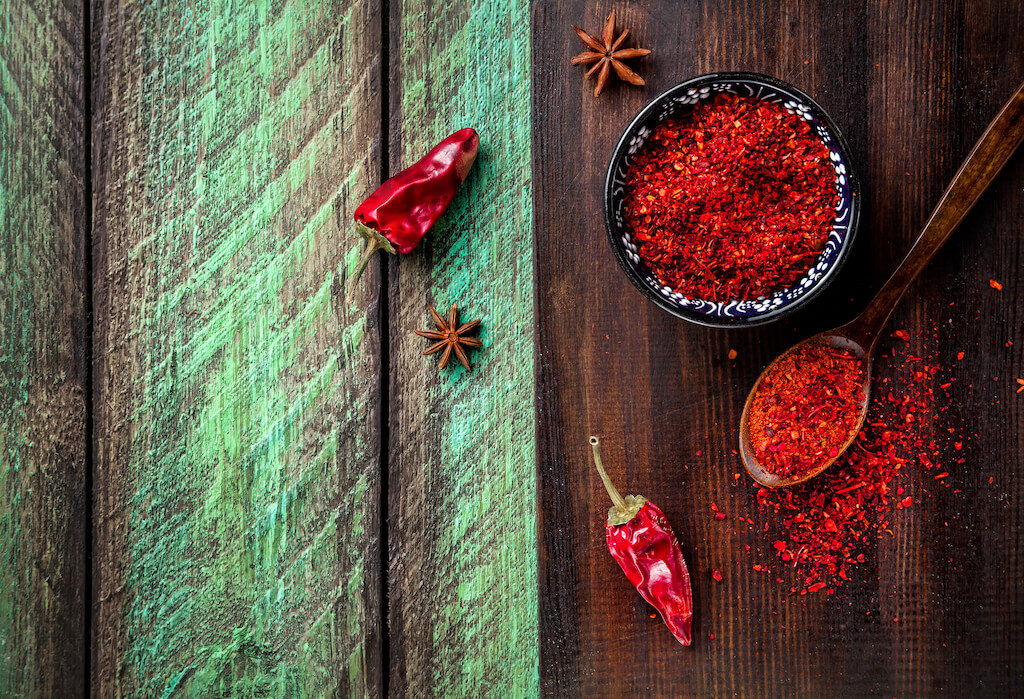Red Chil pepperi and paprika powder on dark cutting board at green wooden table