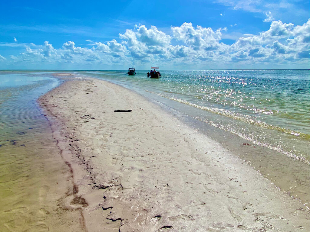 long sand bar with puffy clouds and emerald water