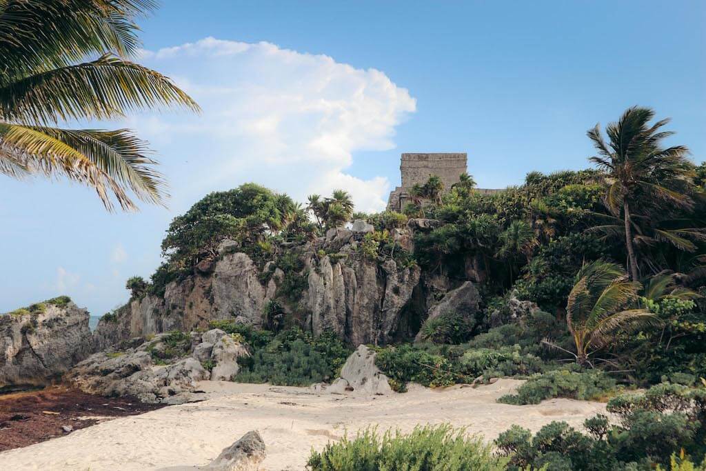 Mayan ruins on a rocky cliff with sandy beach