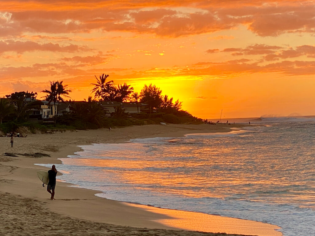 Vivid orange beach sunset with surfer walking