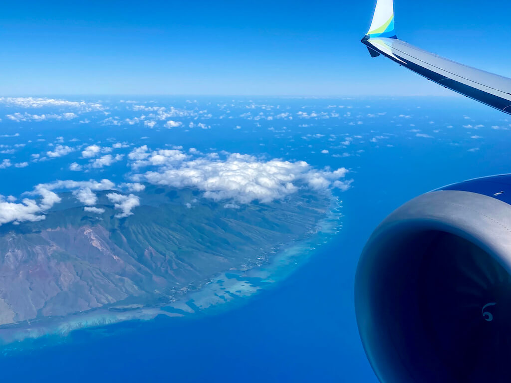 Airplane wing with aerial view of Oahu's green cliffs and white puffy clouds