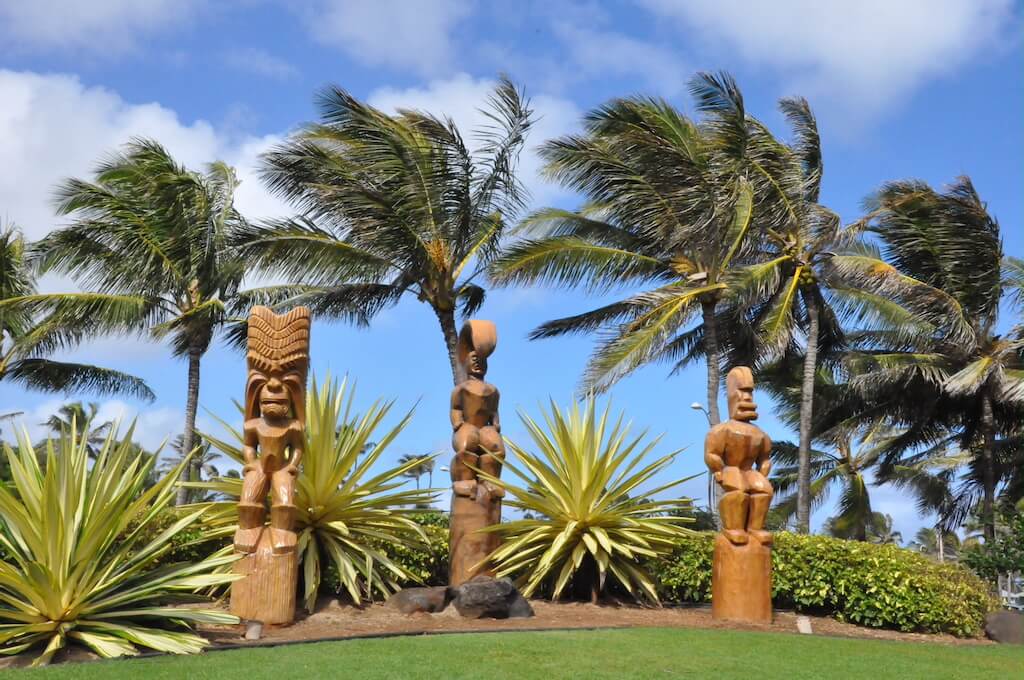 carved wooden Polynesian statues with palm trees blowing in the breeze