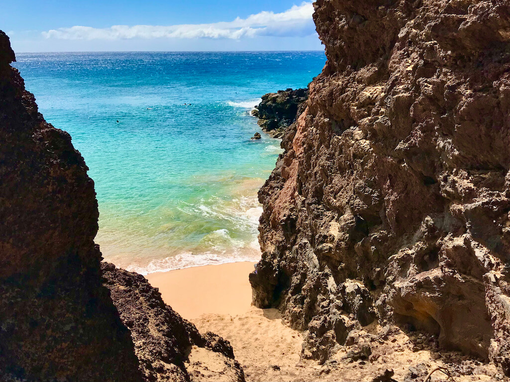 Turquoise ocean and golden sand between rocky lava cliffs in Maui in December