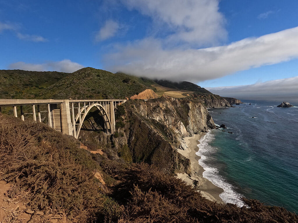 view of Bixby Bridge with surf and blue sky and clouds