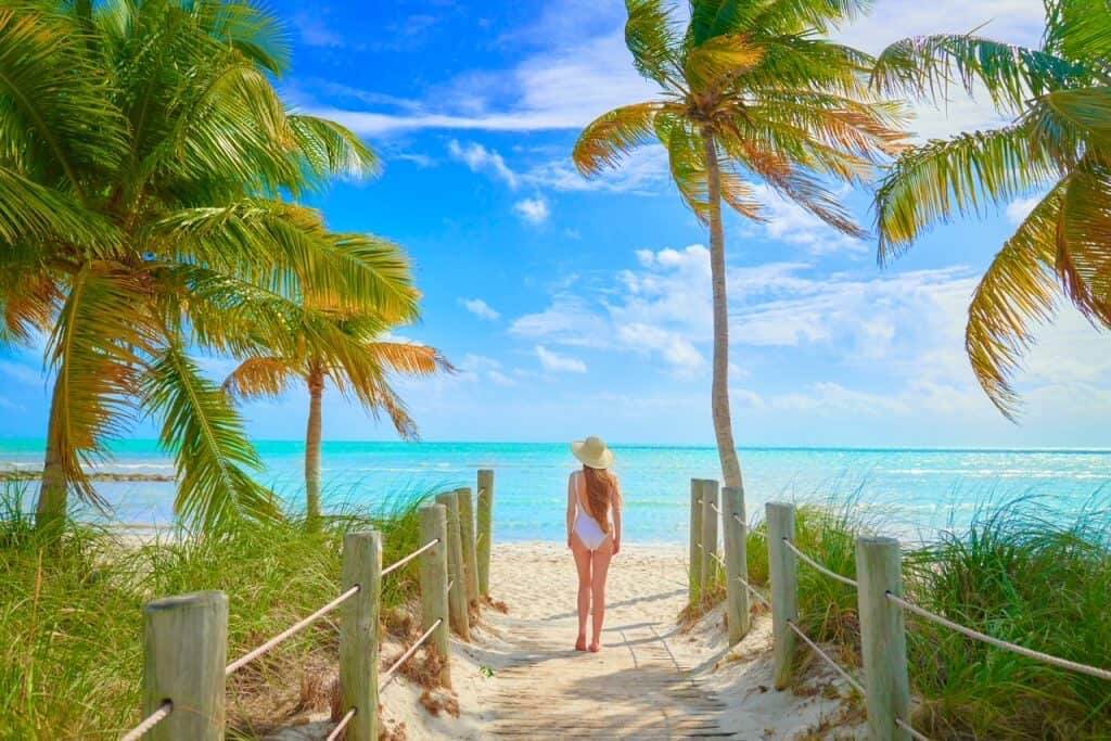 View of girl looking out over blue ocean with windswept palms