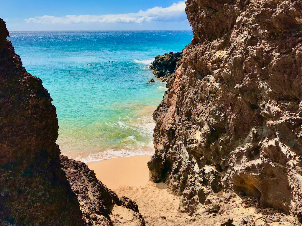 Beautiful Maui beach with rock cliffs, clear blue water, and soft brown sand