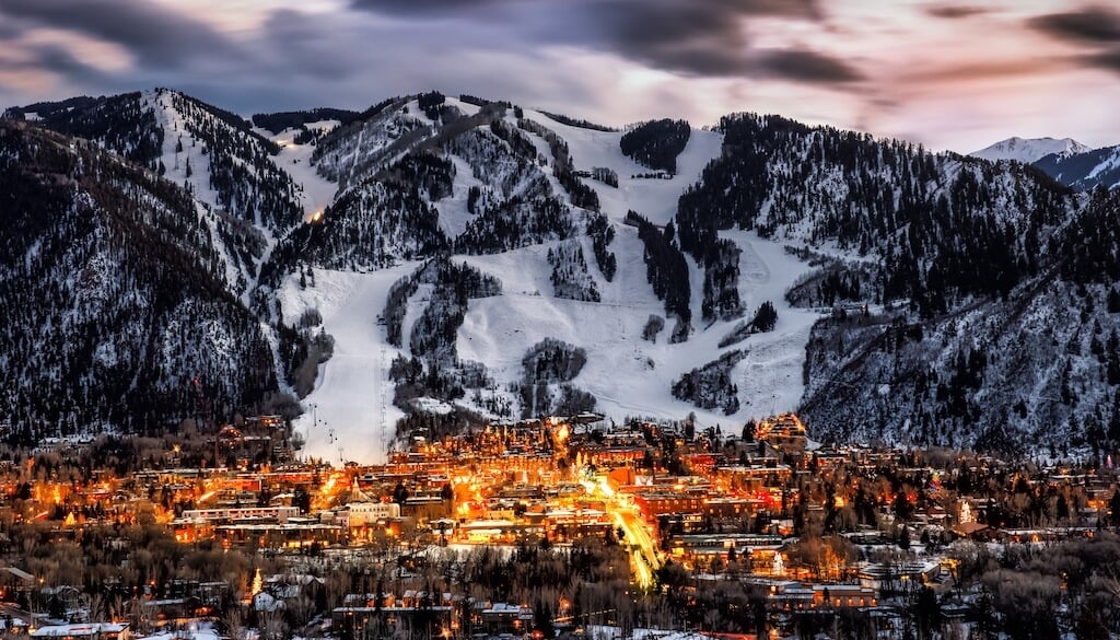 Bright city lights of Aspen at sunset with snowy mountain peaks in background
