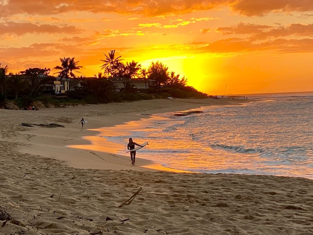 Sunset on Oahu's north shore with a surfer walking the beach